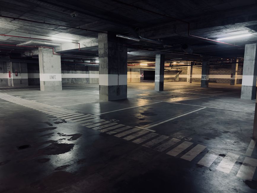 A moody underground parking garage featuring empty spaces and puddles on the floor.