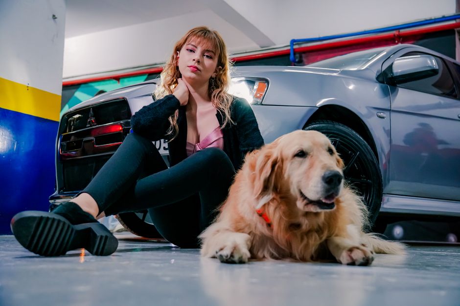 Young woman and golden retriever dog sitting beside a parked car in a garage setting.